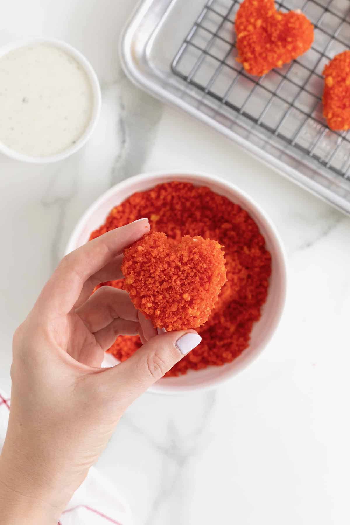 A mozzarella heart being dipped into Cheeto crumbs.