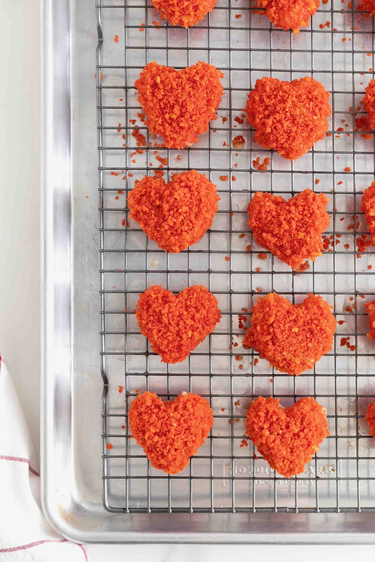A dozen red Flamin' Hot Cheeto Mozzarella hearts on a wire cooling rack over a parchment lined aluminum baking sheet.