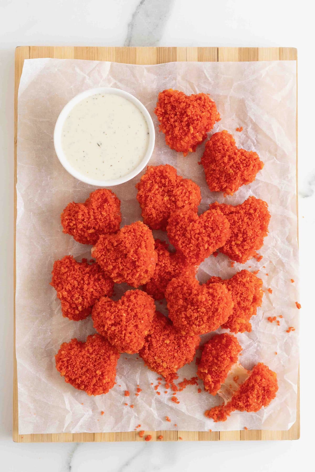 A pile of Flamin' Hot Cheeto Hearts on a parchment lined wood cutting board served a small white dish of spicy ranch dressing.
