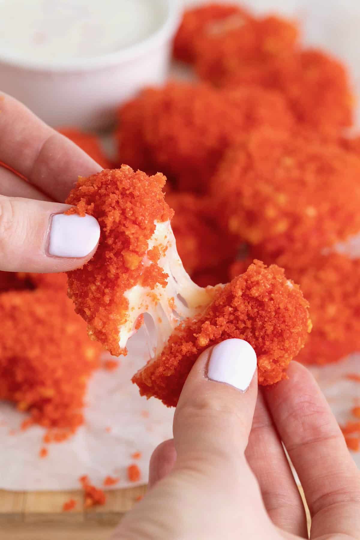 Two hands pulling apart a heart-shaped mozzarella stick coated in red Cheeto coating.