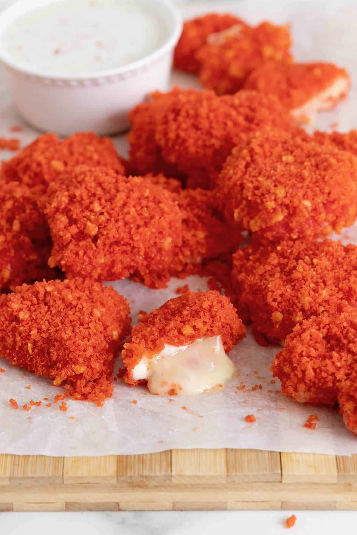 A pile of Flamin' Hot Cheeto Hearts on a white surface next to a small white dish of spicy ranch dressing.