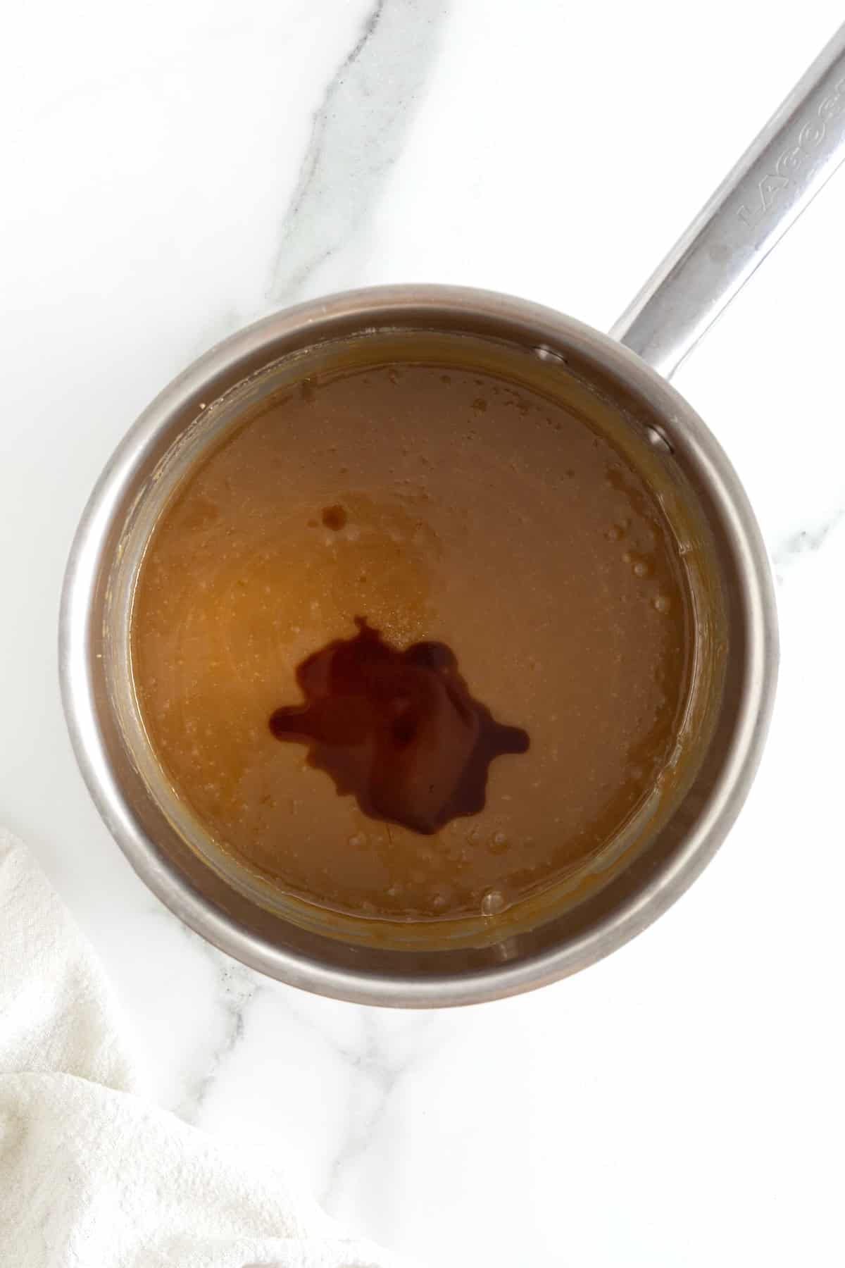 Vanilla extract added to caramel sauce in a light metal saucepan.