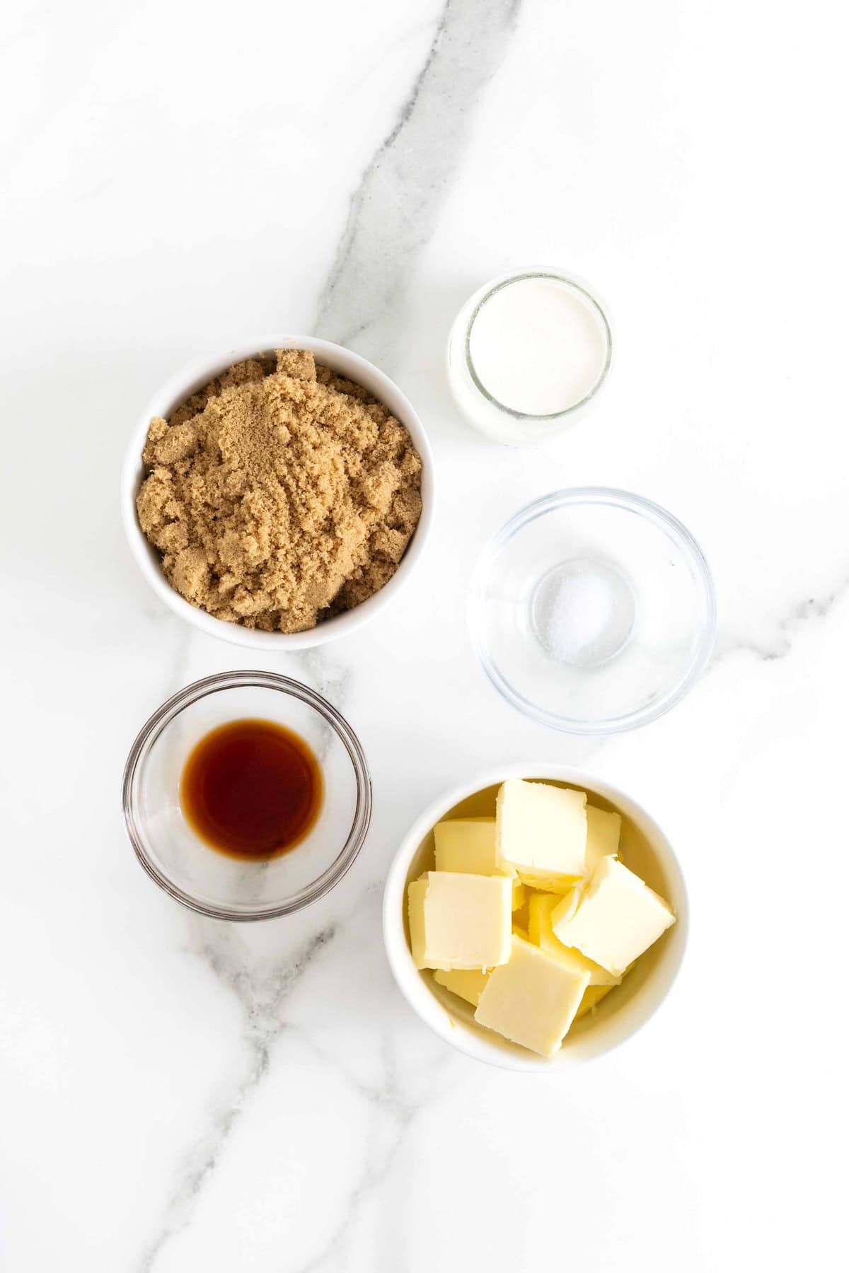 Ingredients to make a simple caramel sauce in small glass dishes on a white marble counter.