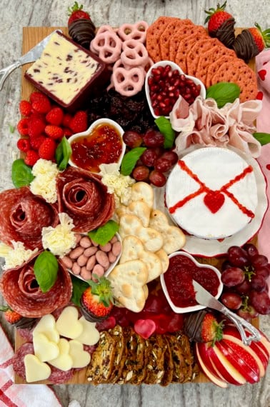 A wood food board decorated with Valentine's Day themed charcuterie items.