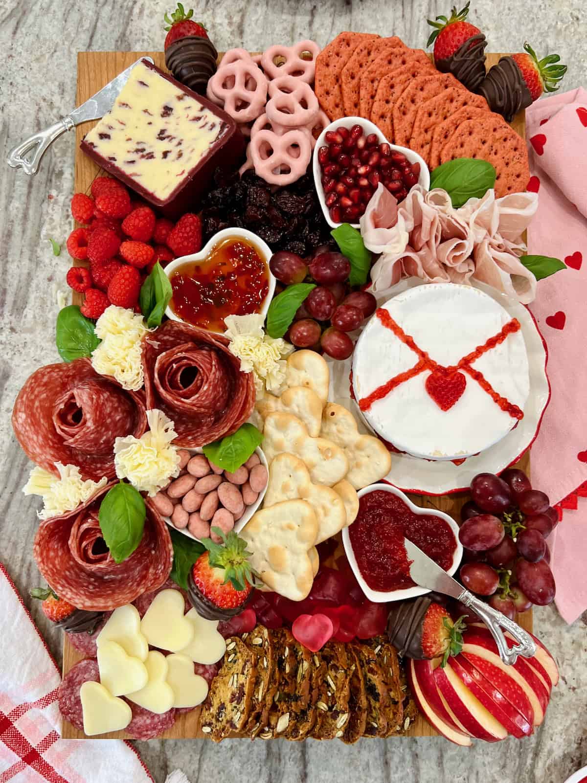A wood food board decorated with Valentine's Day themed charcuterie items.