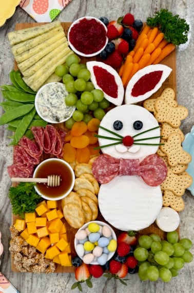 A charcuterie board decorated with a brie Easter bunny, cheese cubes arranged to look like a carrot, salami, crackers, and fruit.