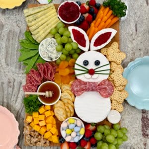 A charcuterie board decorated with a brie Easter bunny, cheese cubes arranged to look like a carrot, salami, crackers, and fruit.