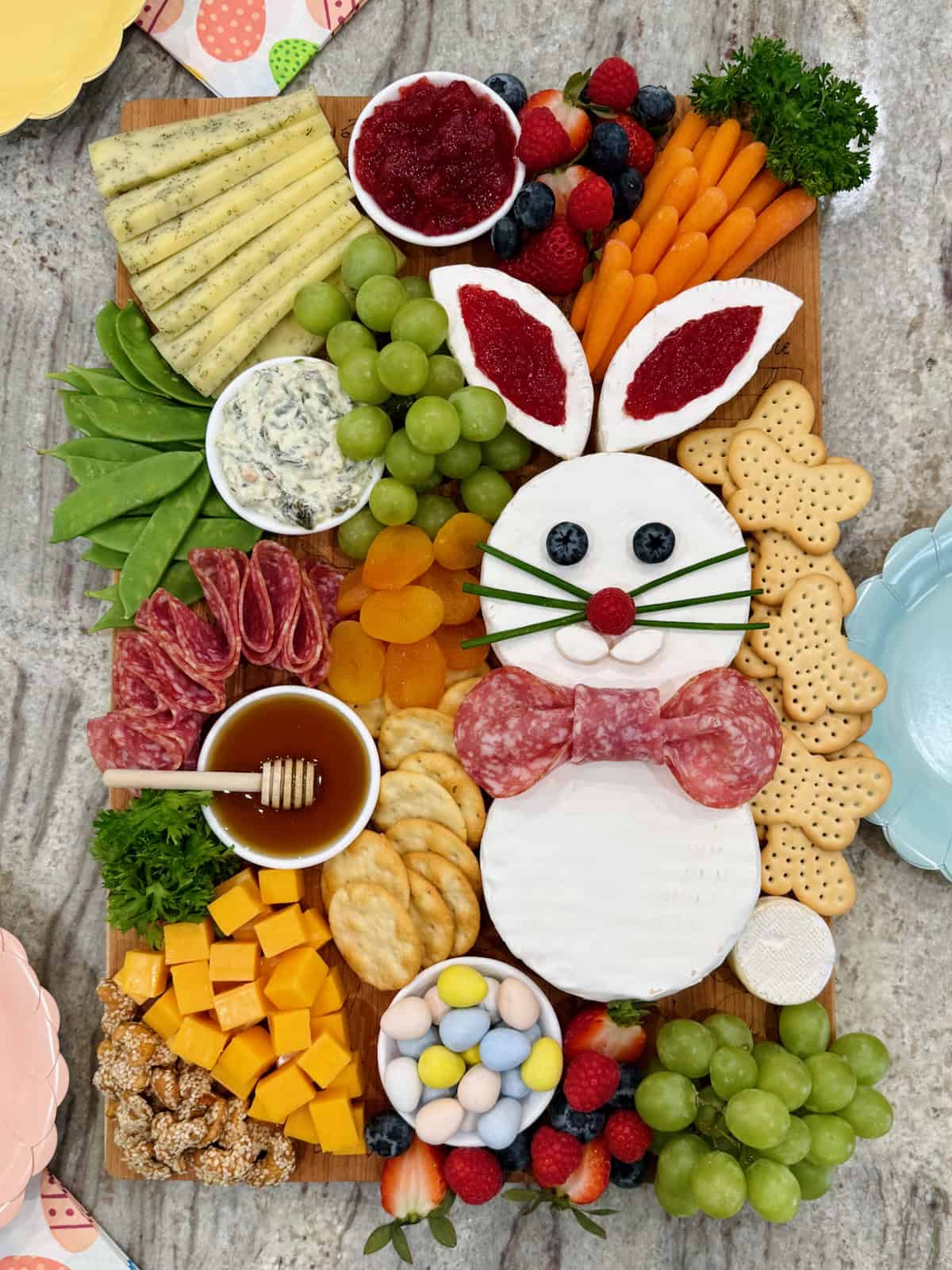 A charcuterie board decorated with a brie Easter bunny, cheese cubes arranged to look like a carrot, salami, crackers, and fruit.