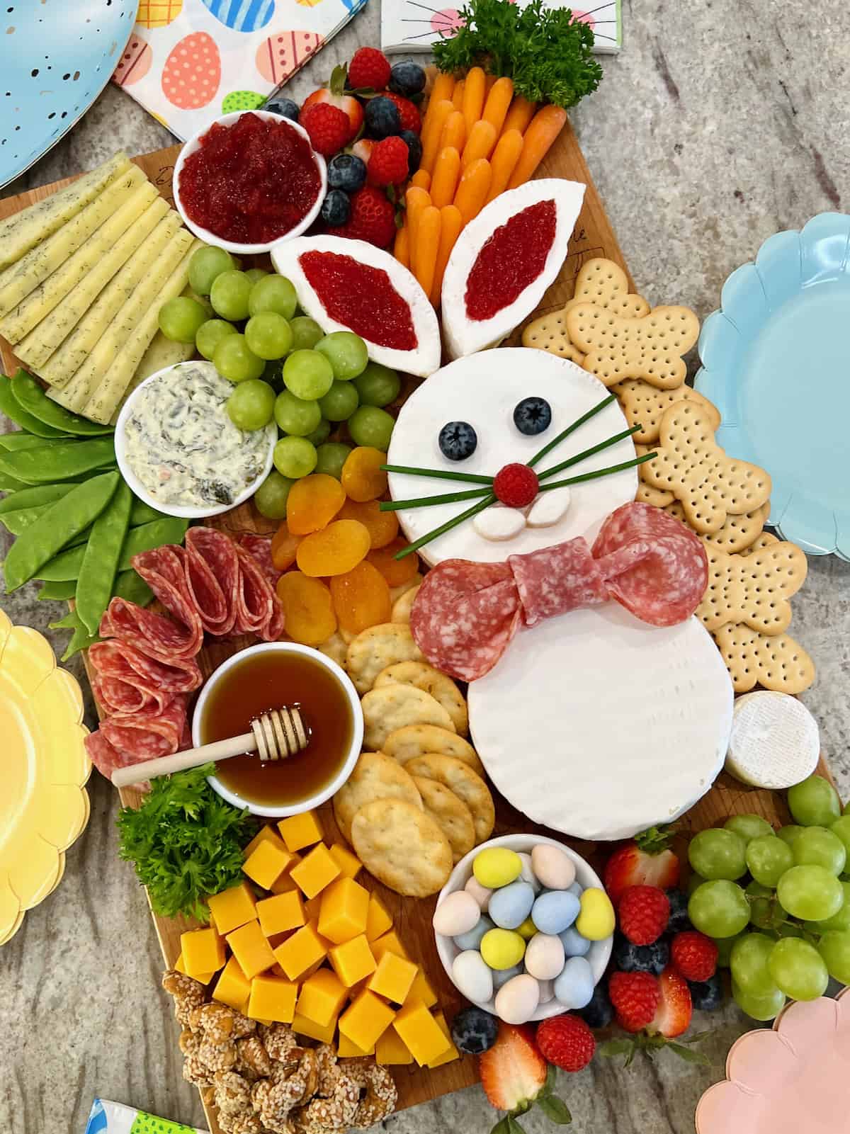 A charcuterie board decorated with a brie Easter bunny, cheese cubes arranged to look like a carrot, salami, crackers, and fruit.