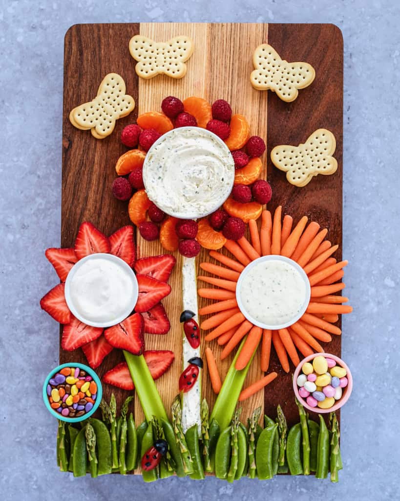 A dark wood food board decorated with foods made to look like flowers growing.