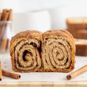 A cinnamon sugar crescent roll loaf on a light wood cutting board. There are cinnamon sticks scattered around it.