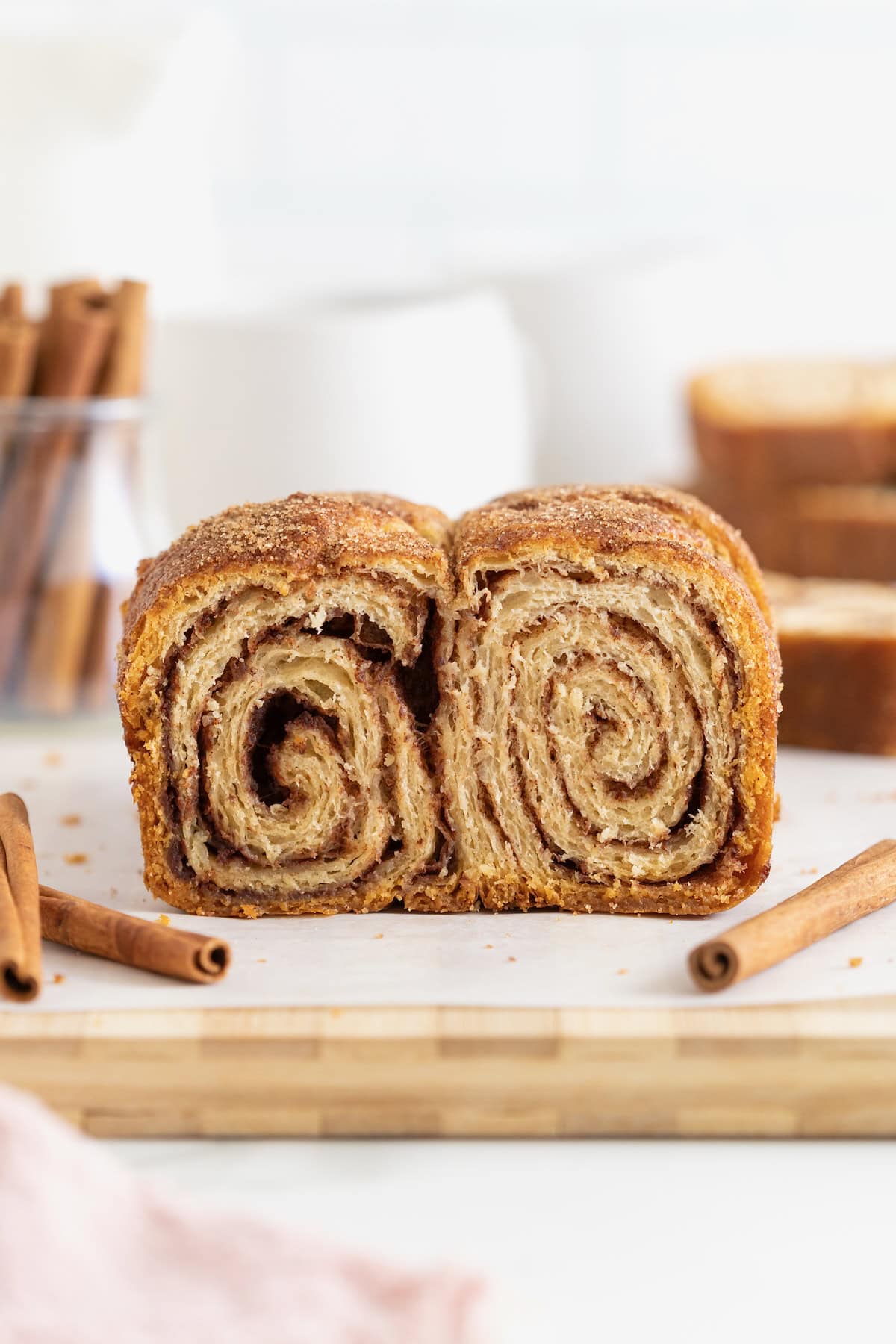A cinnamon sugar crescent roll loaf on a light wood cutting board. There are cinnamon sticks scattered around it.