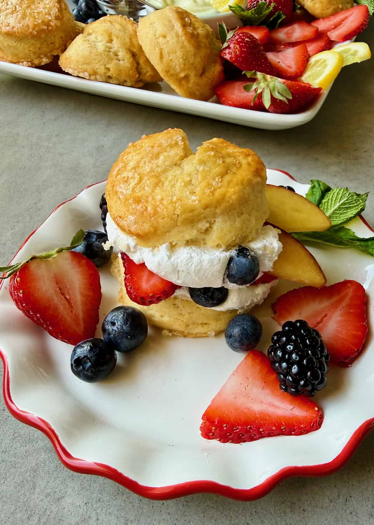 A strawberry and blueberry shortcake on a white fluted dessert plate with a red rim