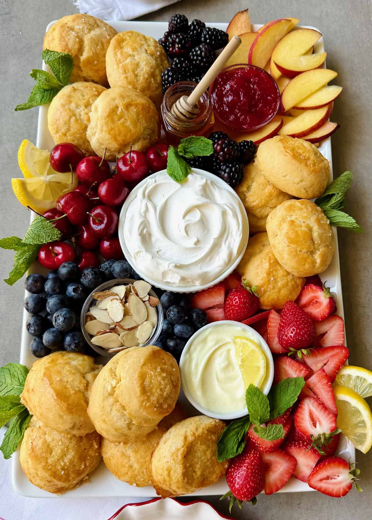 A food board piled with scones, fresh fruits, and small dishes of creamy toppings.