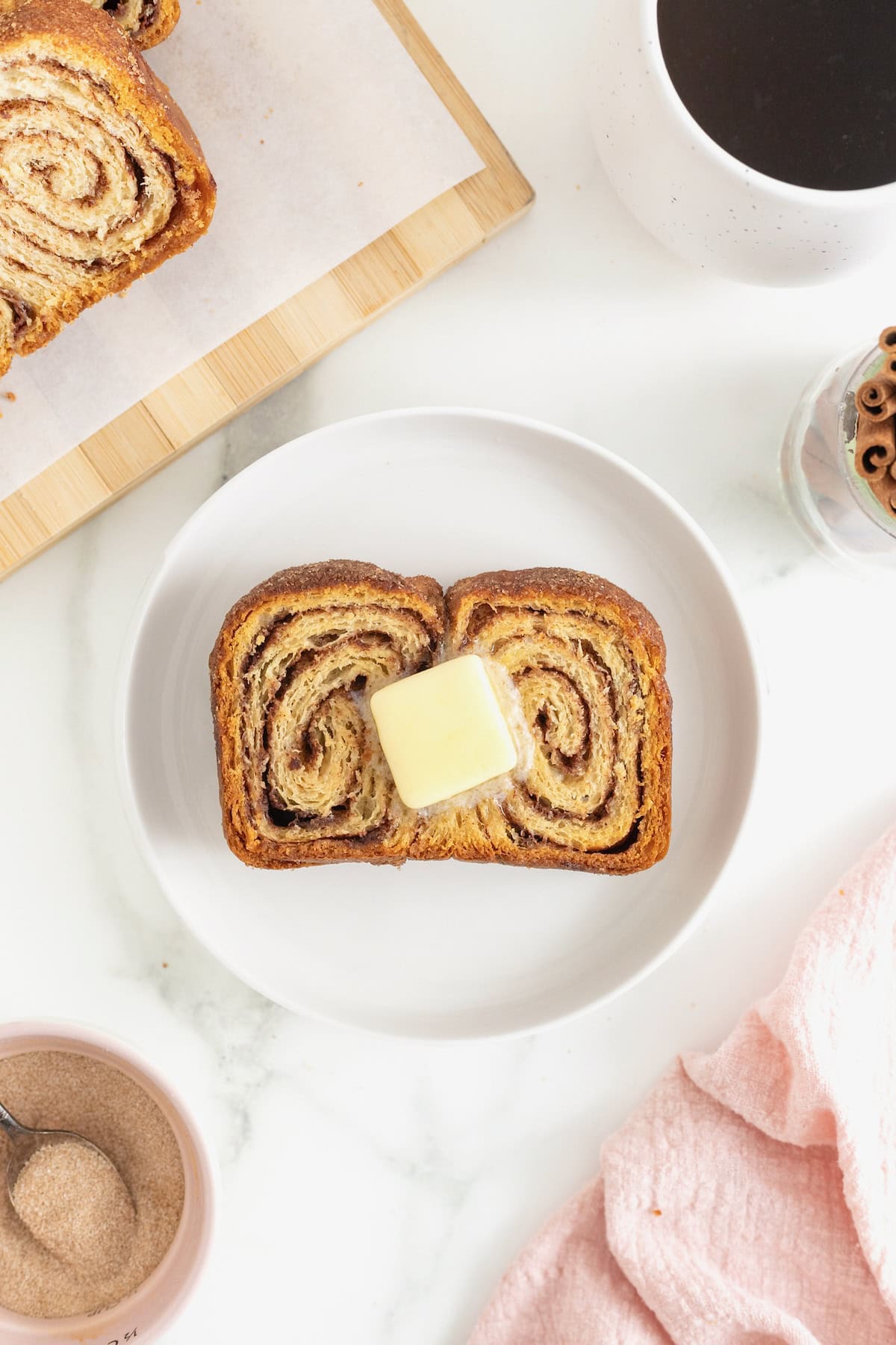 A slice of cinnamon sugar crescent loaf with a pat of butter resting on a small white plate