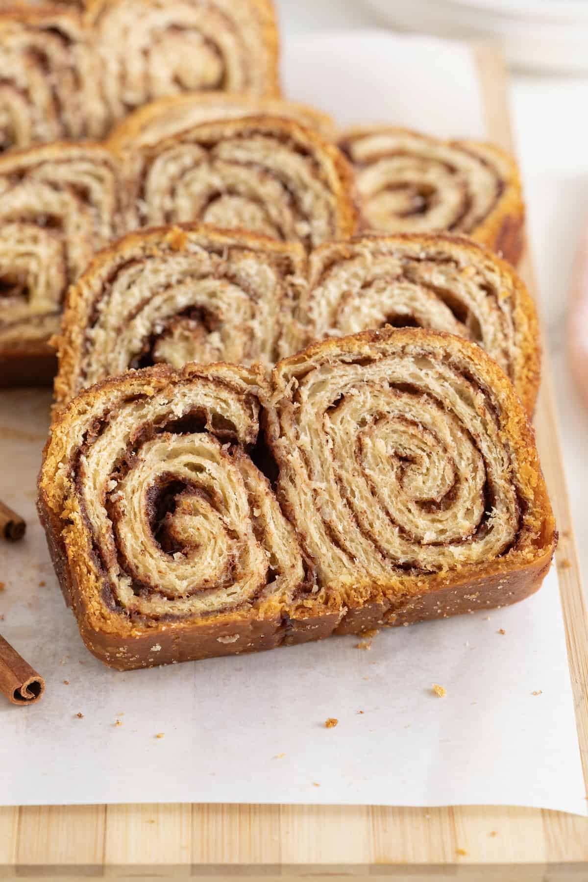 Slices of cinnamon sugar crescent loaf on a parchment lined wood cutting board.