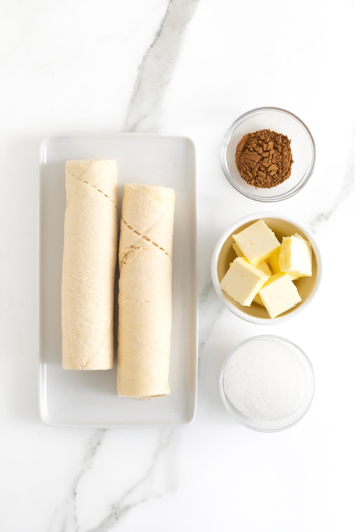 Ingredients to make cinnamon sugar crescent loaf in small dishes on a white marble counter.