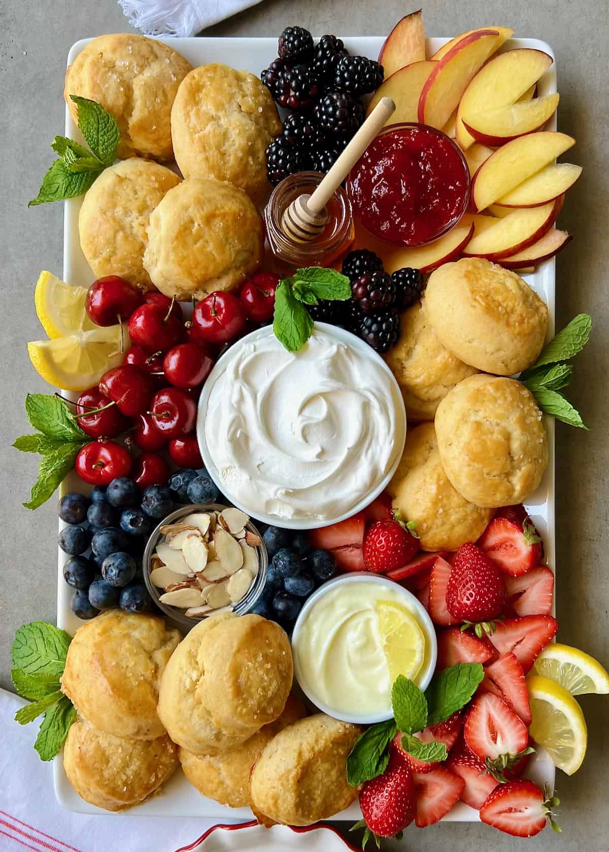 A food board piled with scones, fresh fruits, and small dishes of creamy toppings.