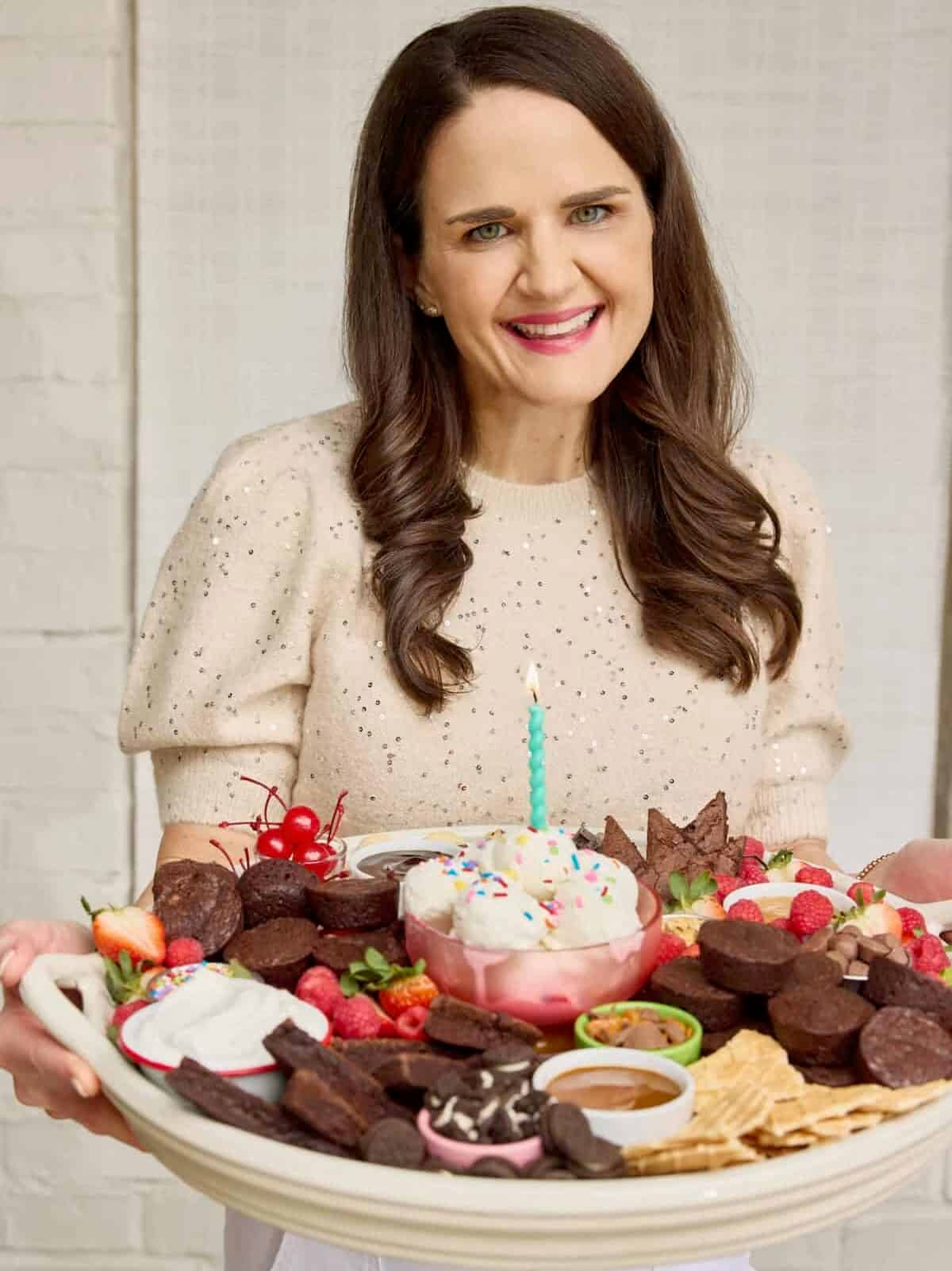 Maegan Brown wearing a pale, short sleeve sweater holding a tray of brownie bites and dips.