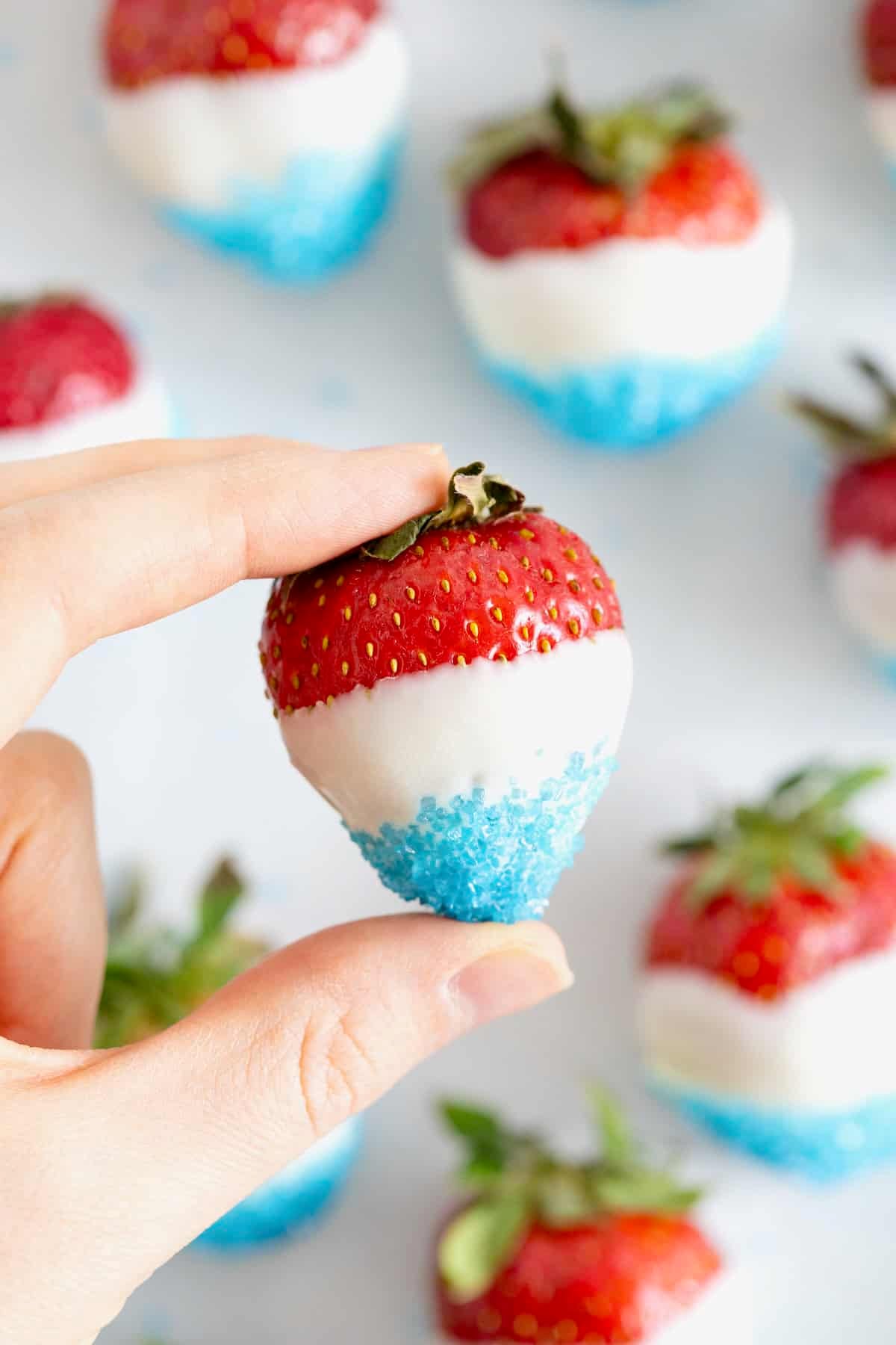 A hand holding a red white and blue strawberry.
