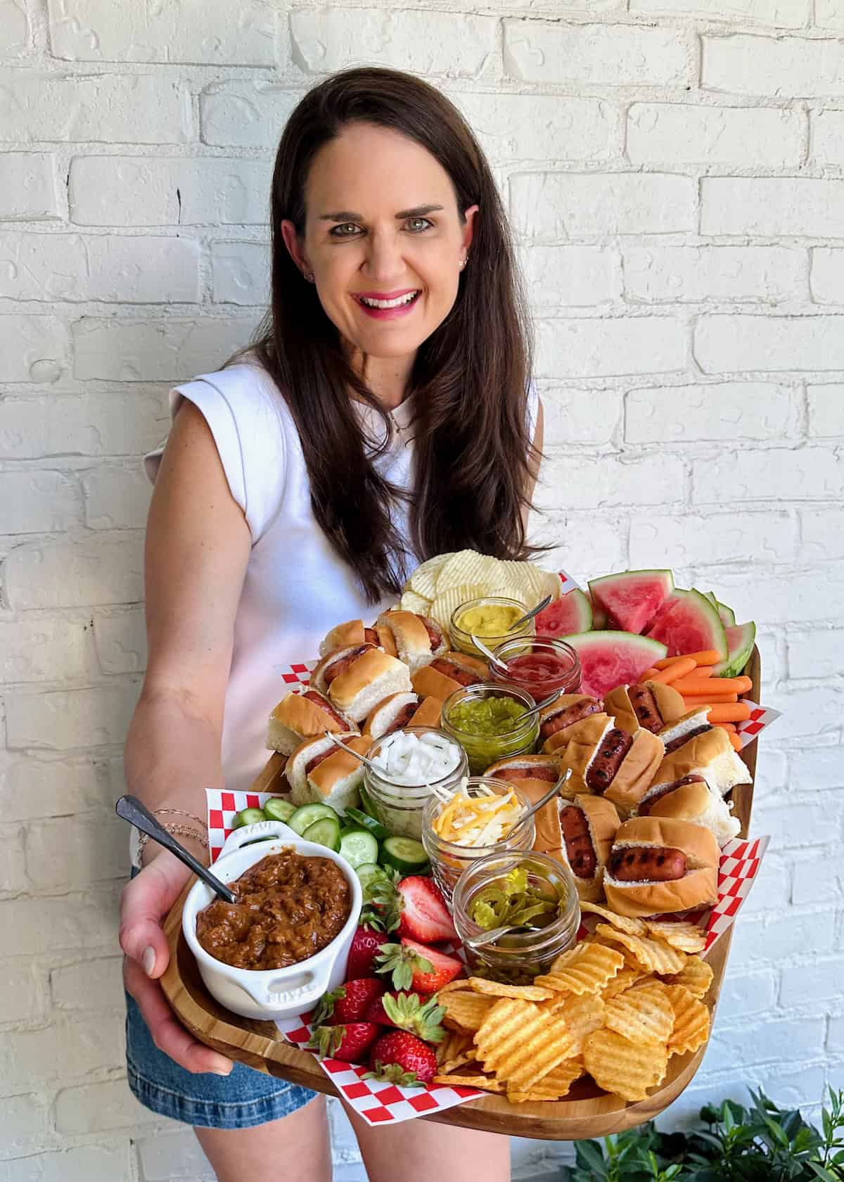 Maegan Brown wearing a white short sleeve shirt holding a mini hotdog food board.