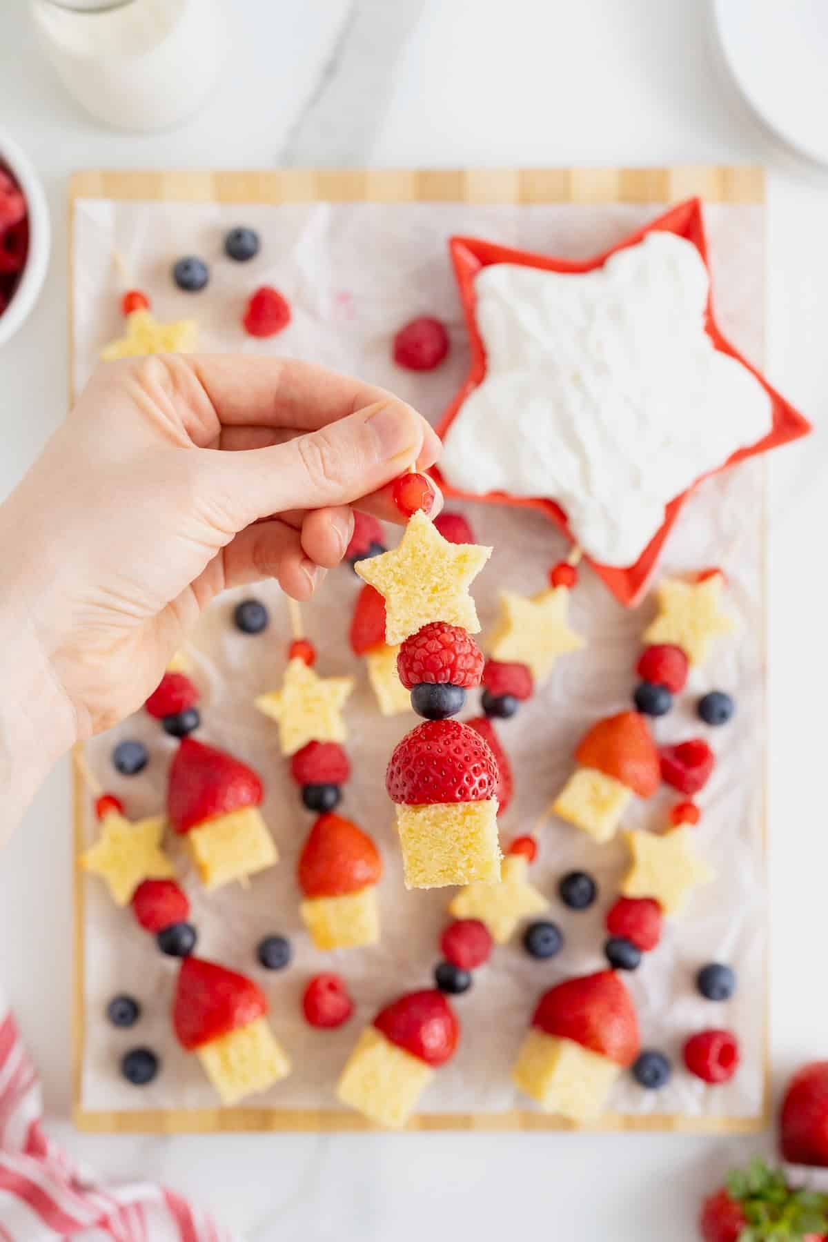 A hand holding a skewer made of poundcake and berries.