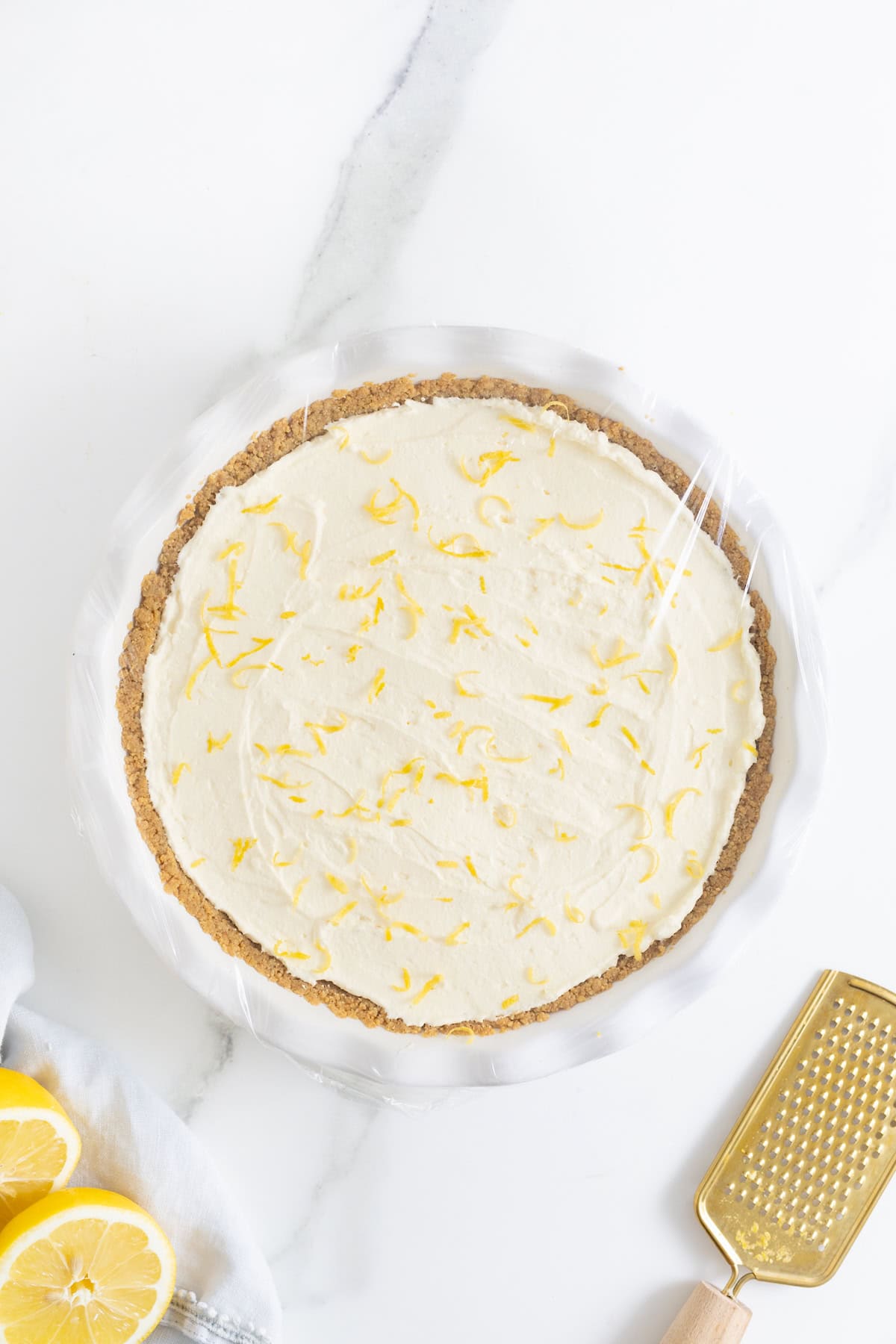 A frozen lemonade pie covered in plastic wrap.