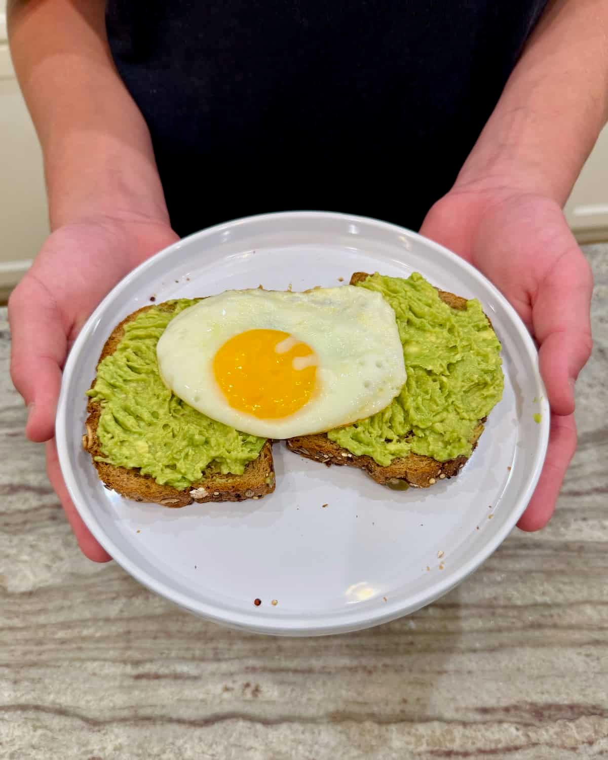 Two pieces of avocado toast topped with a fried egg on a white rimmed plate.