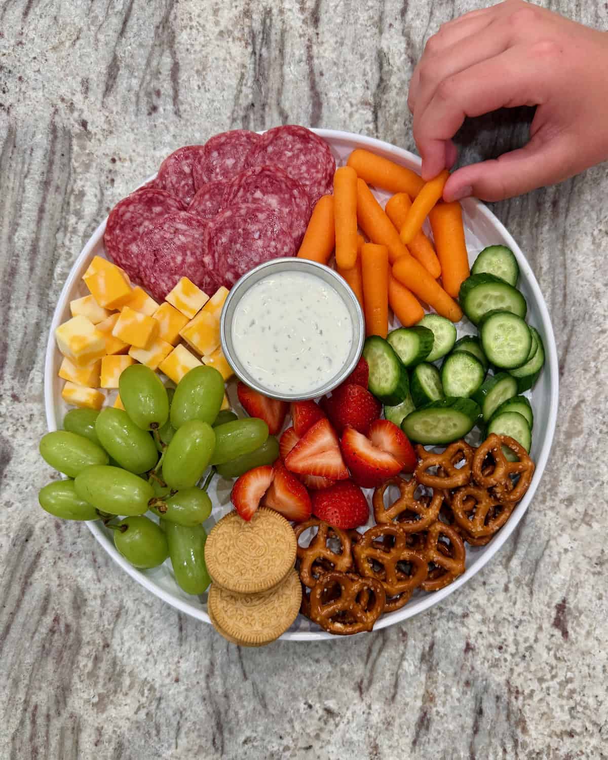 A hand selecting a baby carrot from a snack plate.