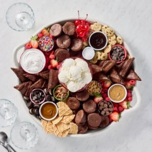 A large round serving tray filled with brownie bites, brownie triangles, scoops of vanilla ice cream, and various toppings.