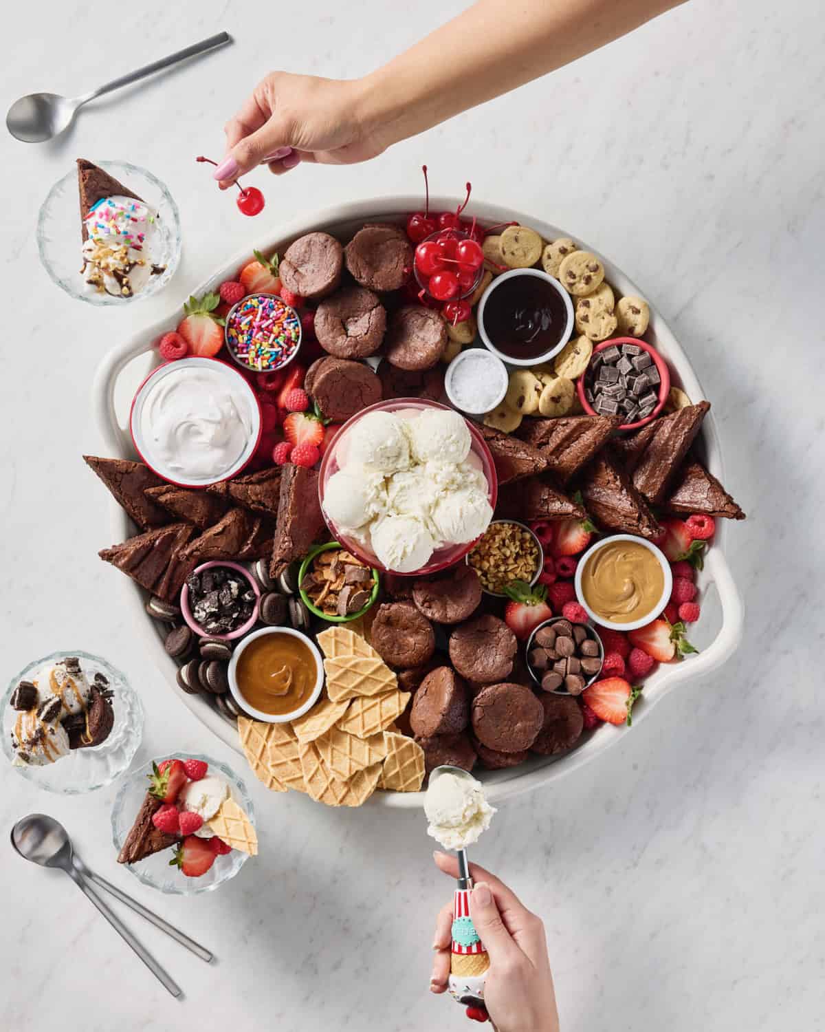 A large round serving tray filled with brownie bites, brownie triangles, scoops of vanilla ice cream, and various toppings.