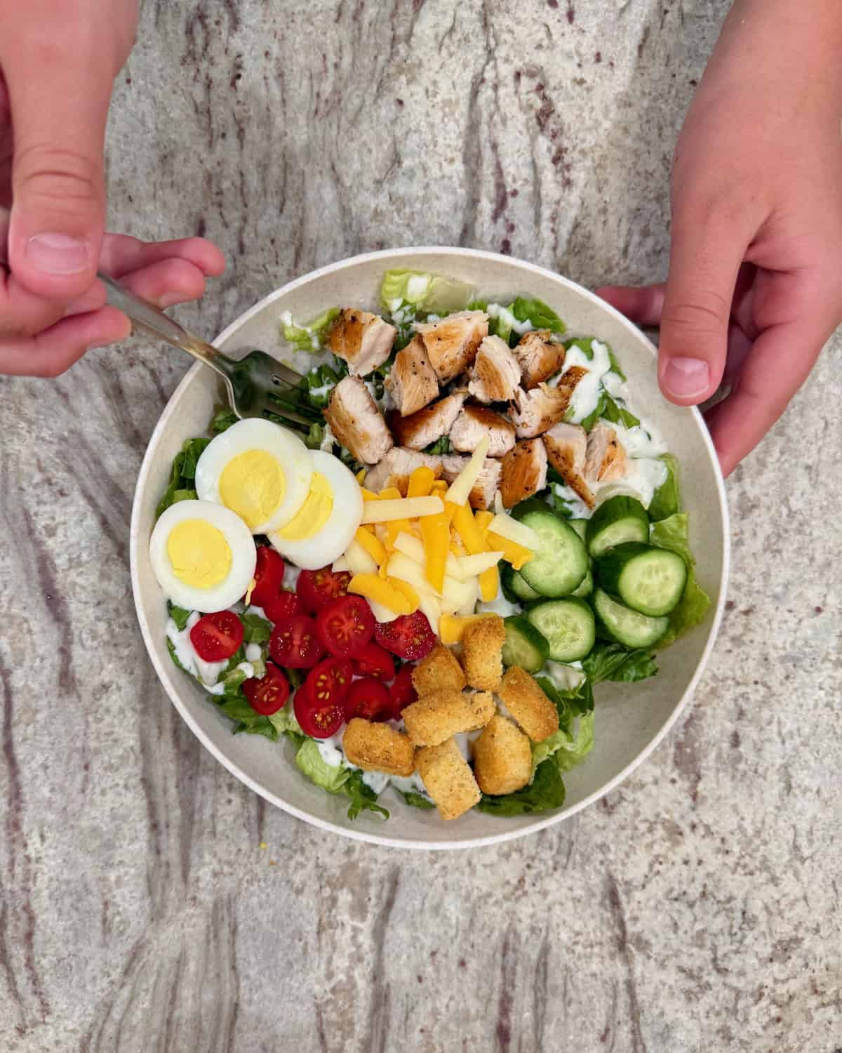 Hands holding a fork and a plate of salad.