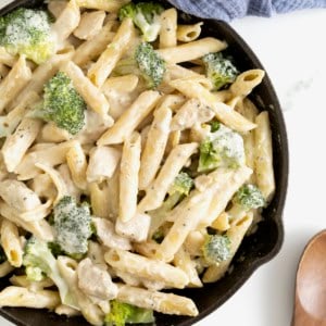 A cast iron skillet of penne pasta and broccoli covered in a cream sauce.
