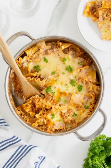 A stainless steel skillet with lasagna noodles and melting cheese sprinkled with parsley.