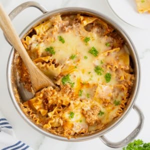 A stainless steel skillet with lasagna noodles and melting cheese sprinkled with parsley.