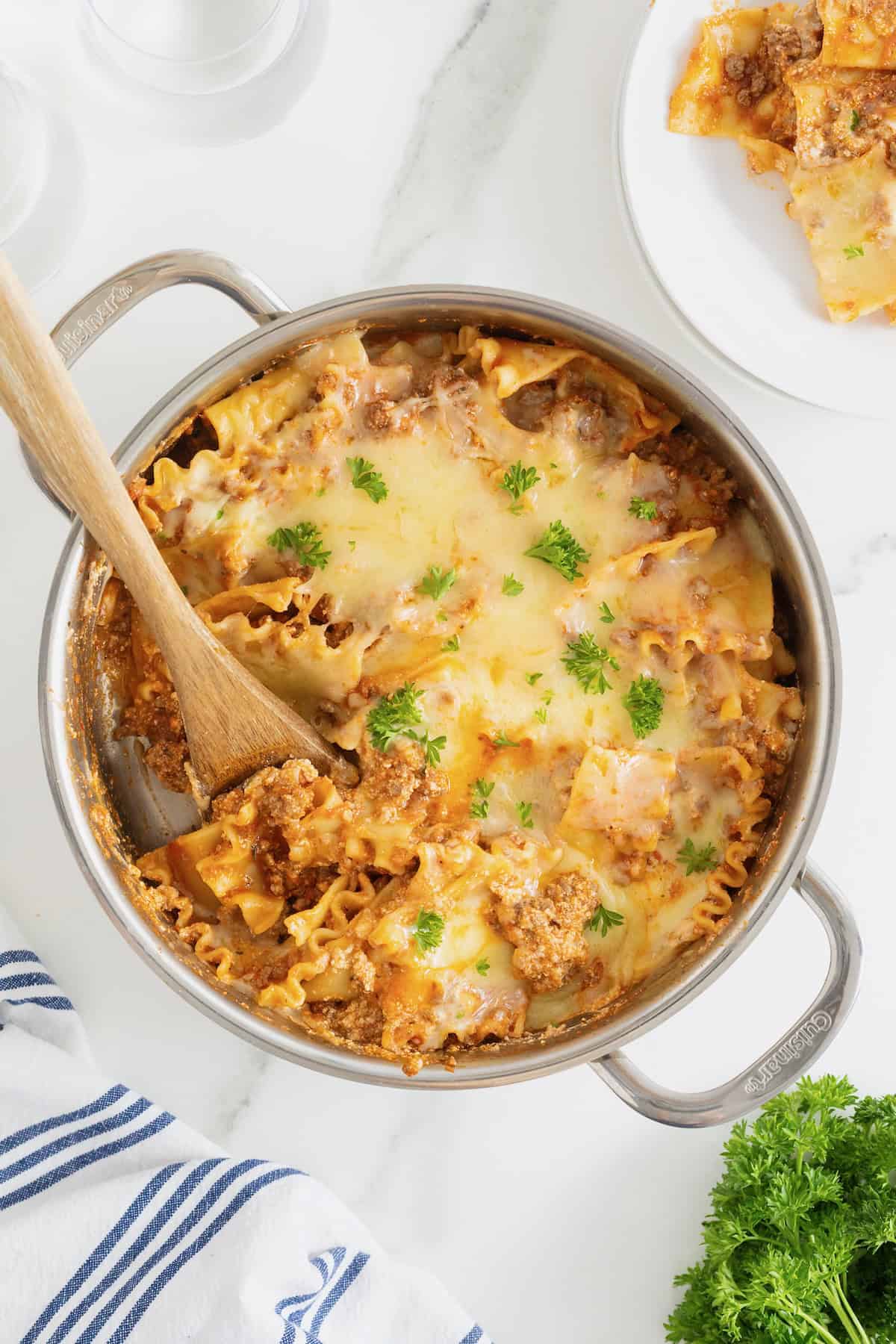 A stainless steel skillet with lasagna noodles and melting cheese sprinkled with parsley.