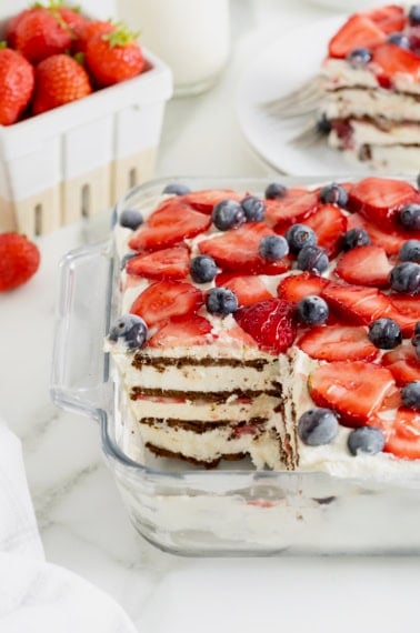 An ice cream sandwich cake in a glass dish topped with fresh strawberries and blueberries.