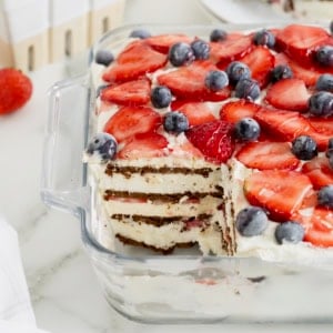An ice cream sandwich cake in a glass dish topped with fresh strawberries and blueberries.