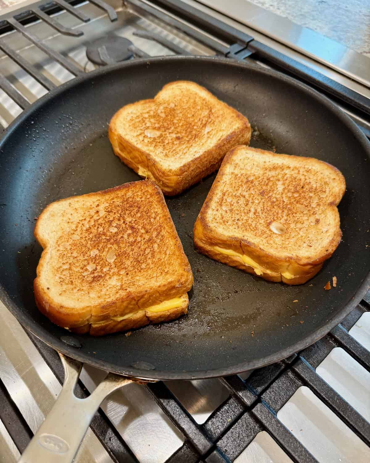 A dark skillet with three grilled cheese sandwiches.