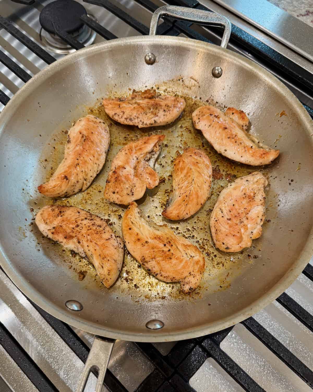 A stainless steel skillet with cooked chicken tenderloins.