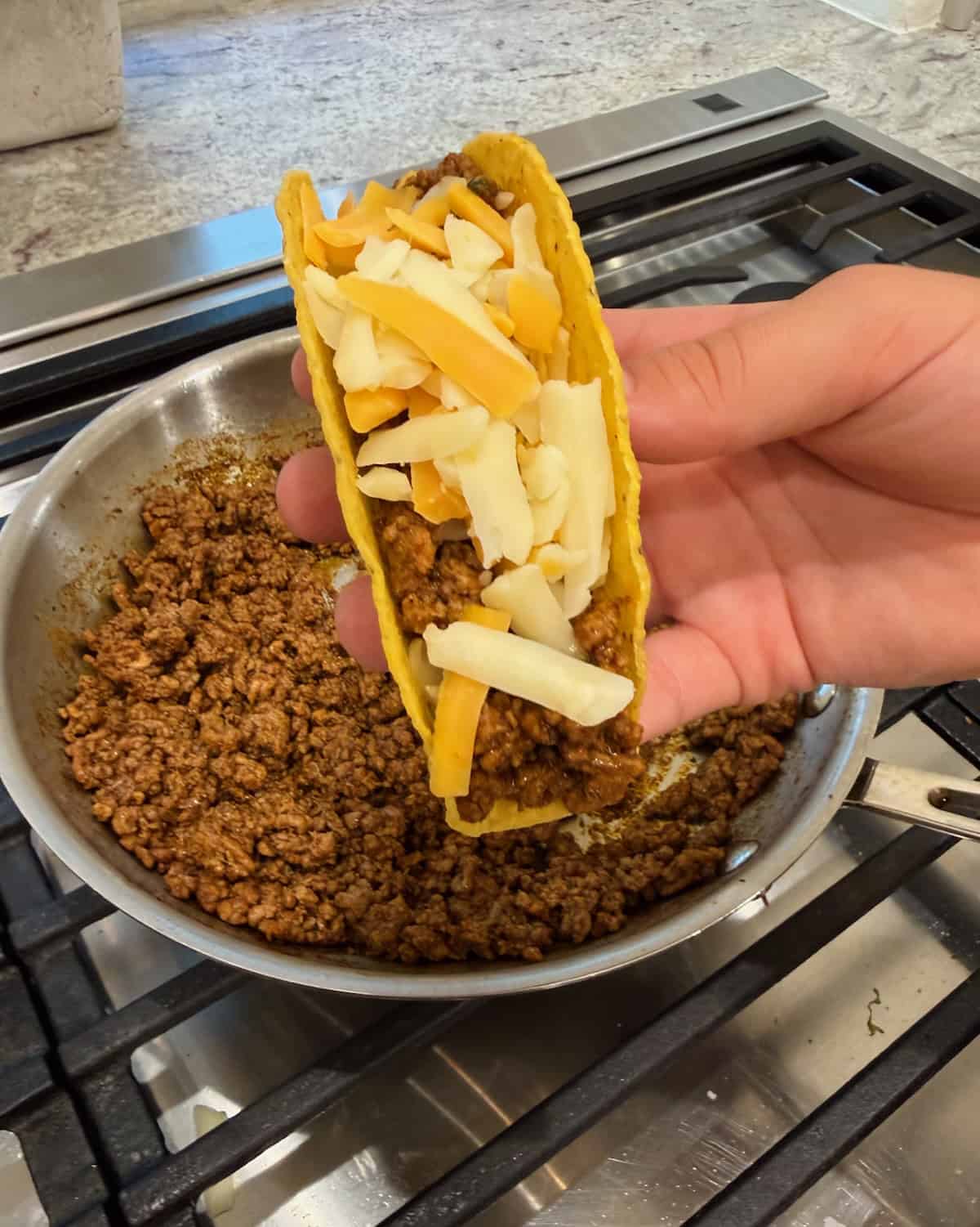 A hand holding a hard shell taco filled with ground beef and topped with cheese.