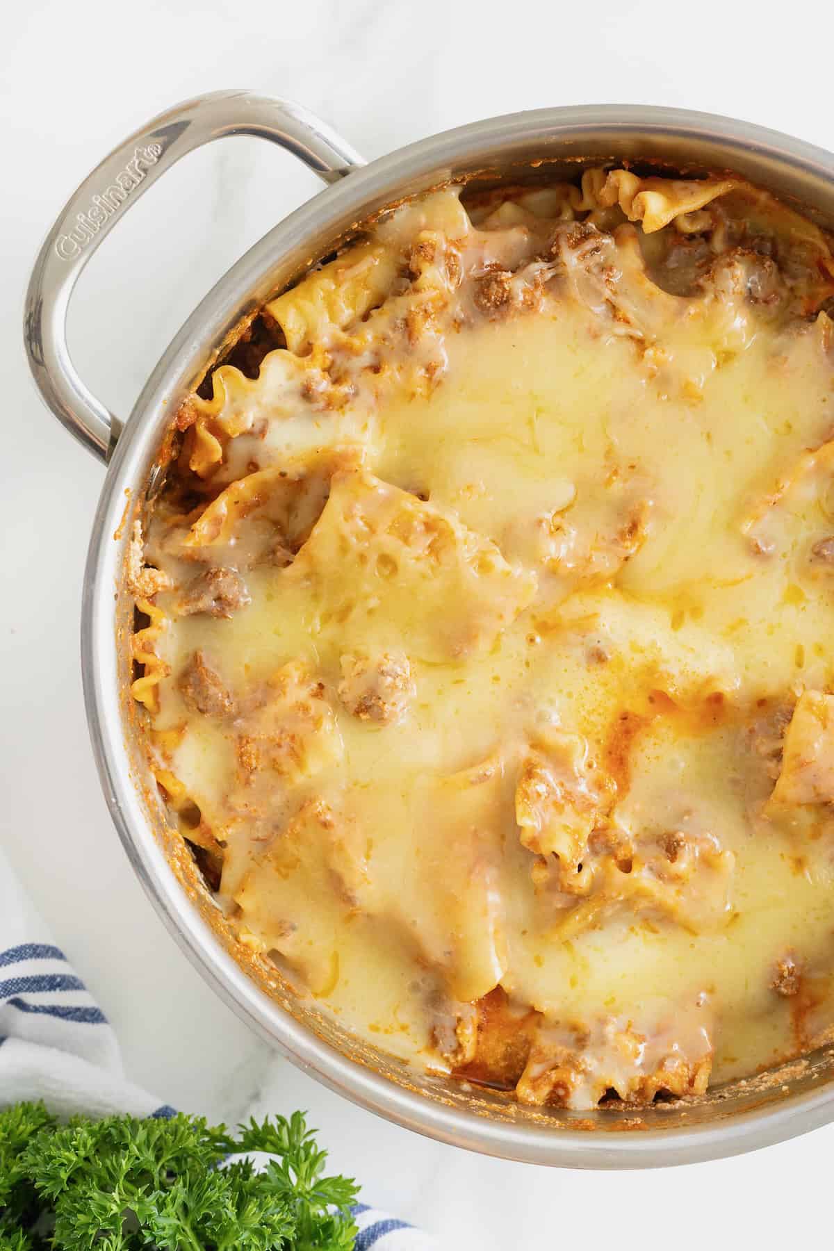 A deep stainless steel skillet with lasagna noodles and melting cheese.