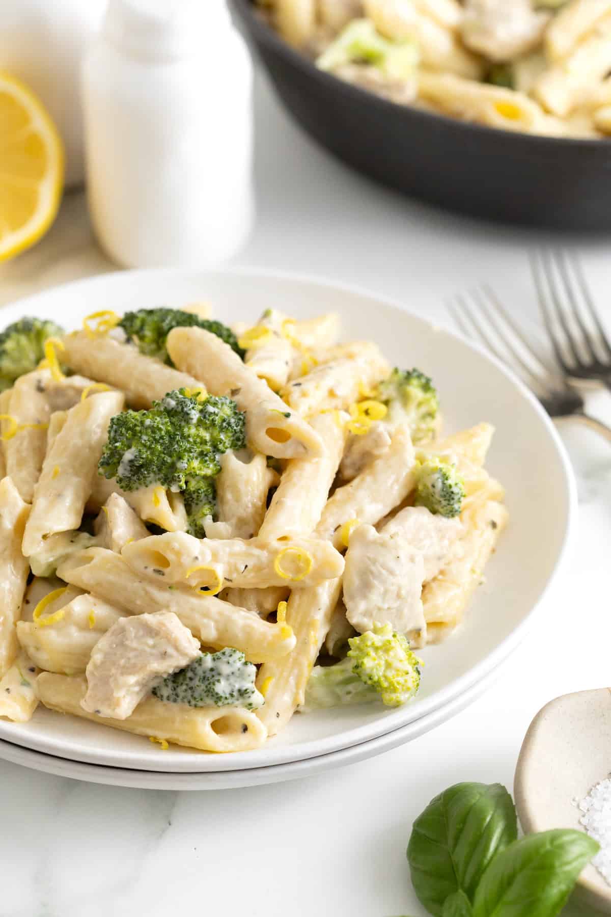 A white dinner plate filled with a creamy pasta dish with broccoli florets and chicken in a creamy sauce.