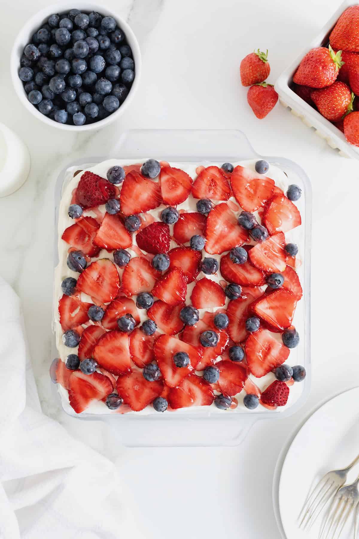 An ice cream sandwich cake in a glass dish topped with fresh strawberries and blueberries.