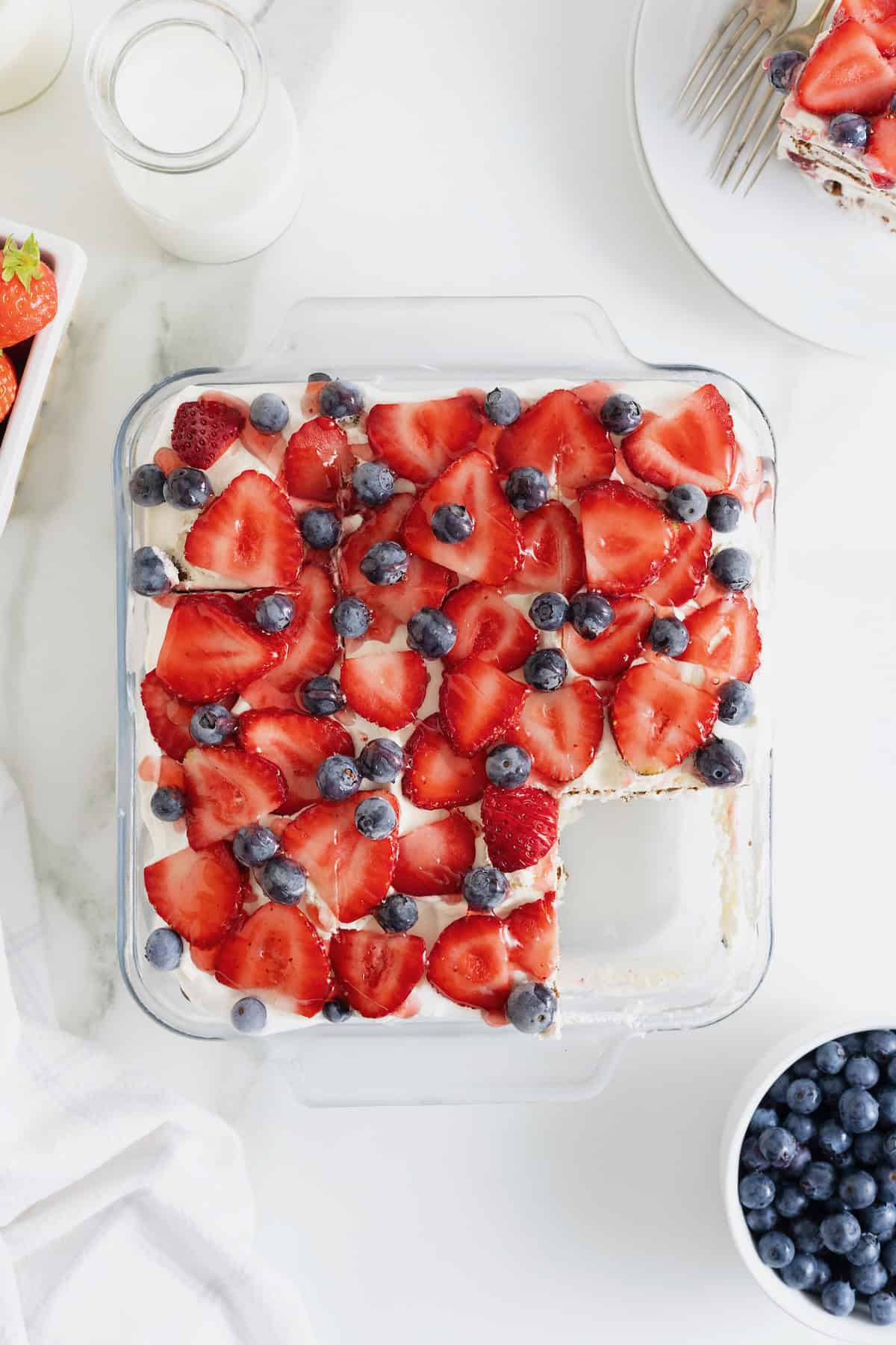 An ice cream sandwich cake in a glass dish topped with fresh strawberries and blueberries.