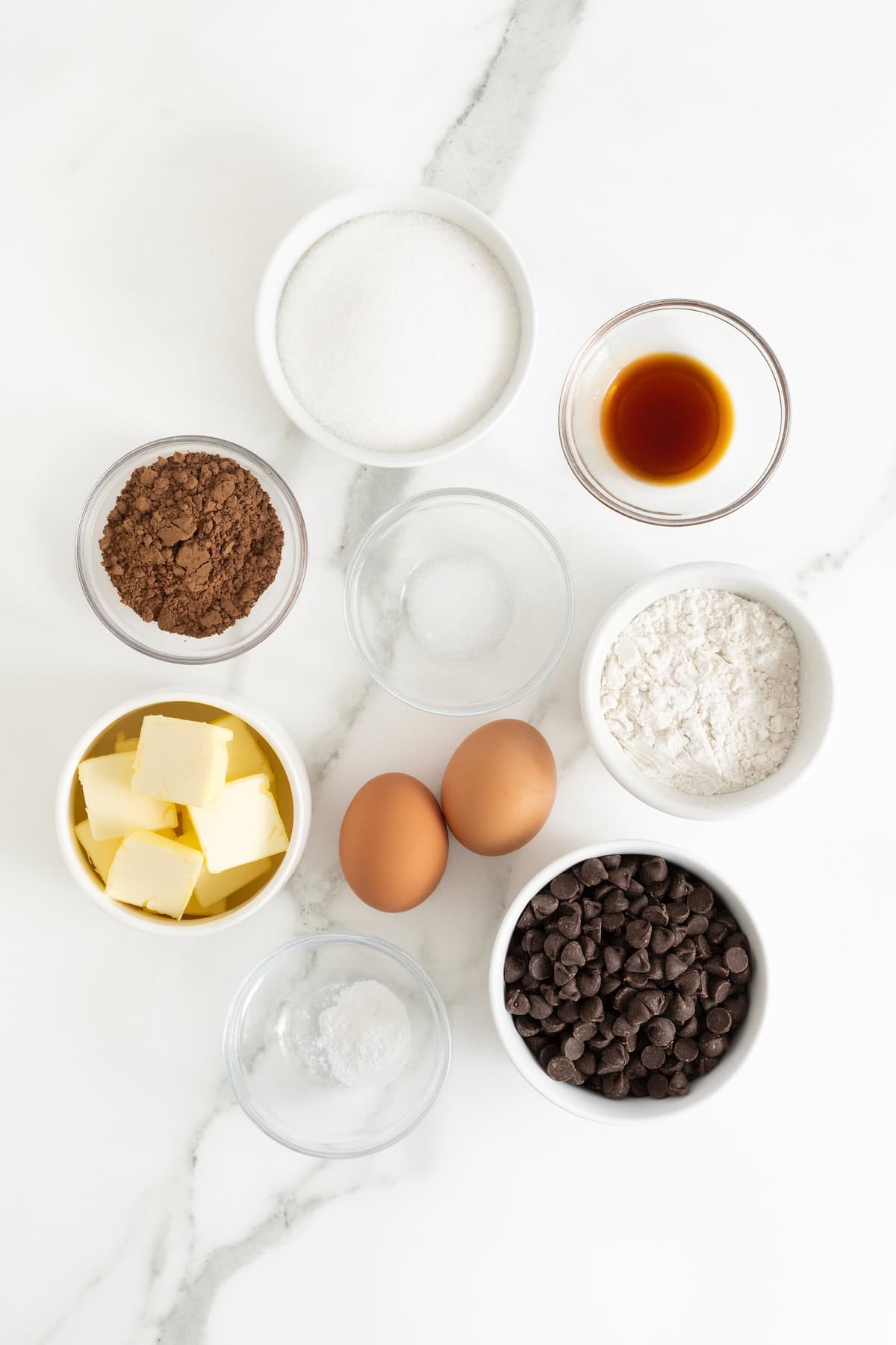 Ingredients to make a skillet brownie in small glass dishes on a white marble counter.