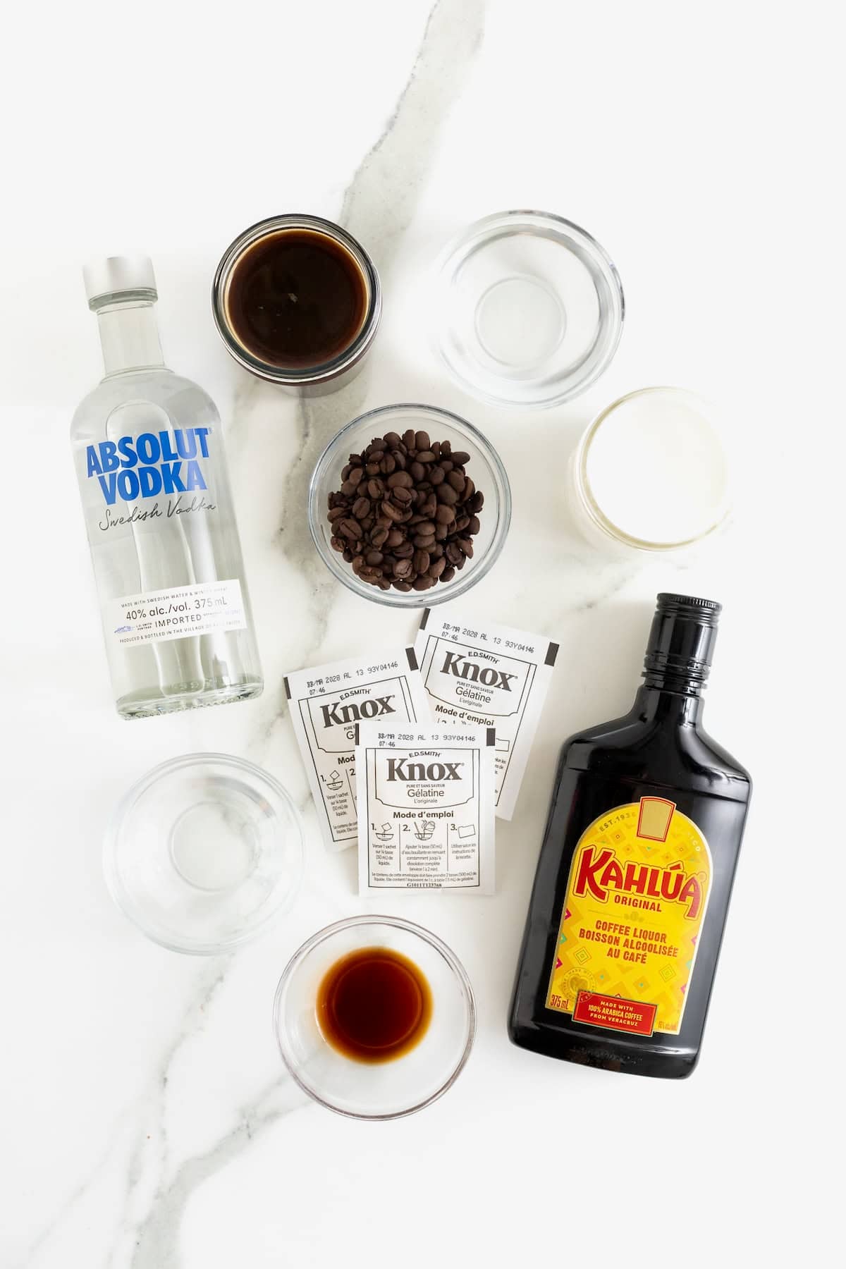 Ingredients to make espresso martini shots on a white marble counter.