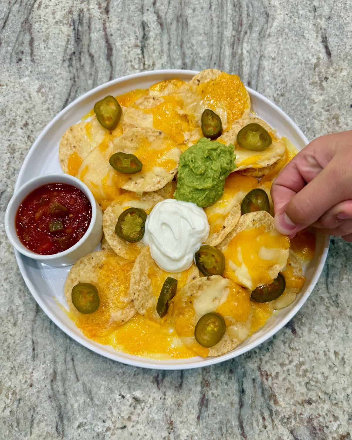A large white rimmed plate of microwave nachos and a small container of salsa.