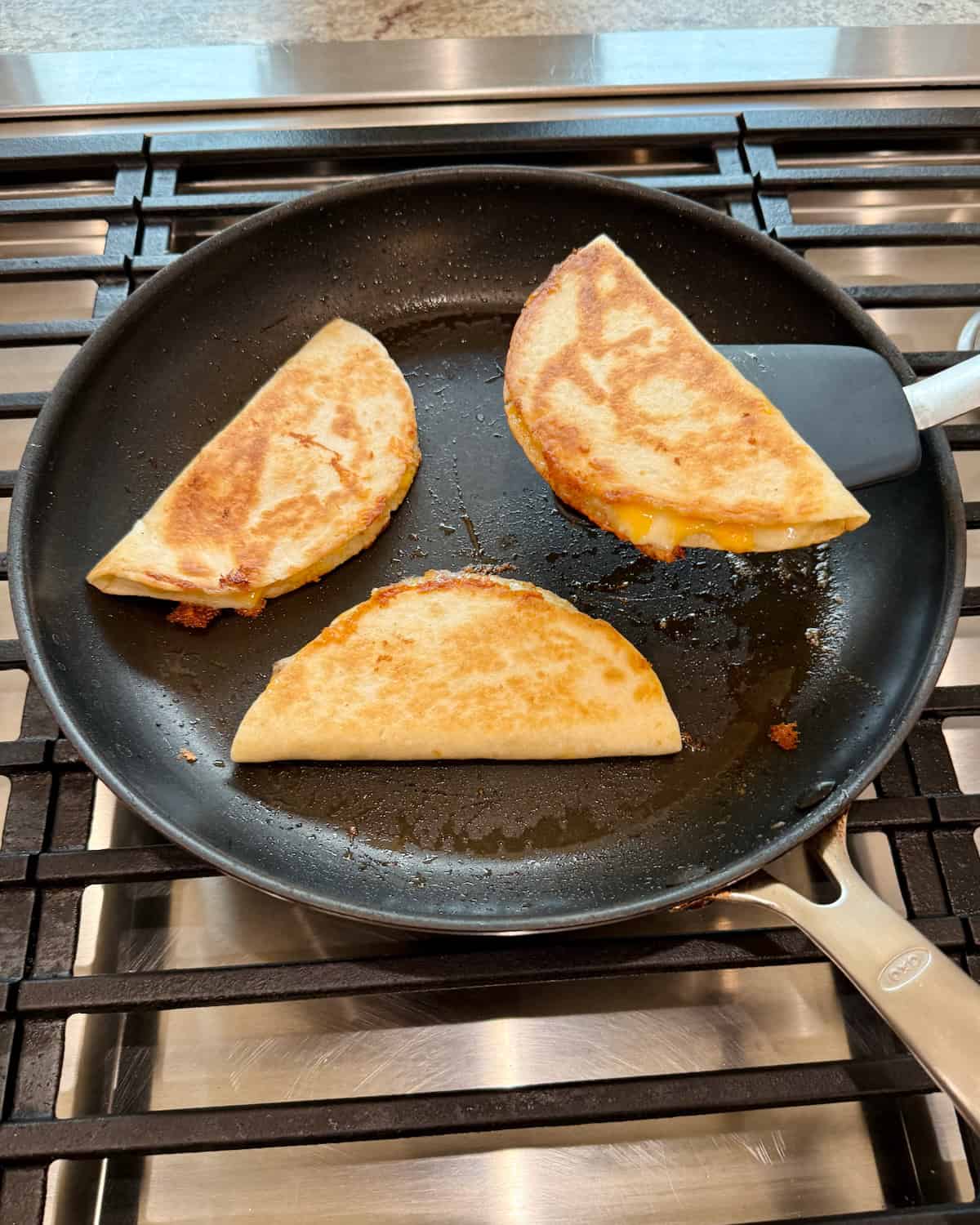 Three quesadillas in a dark skillet on a stove.