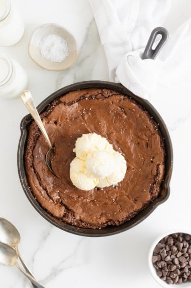 A skillet brownie topped with several scoops of vanilla ice cream.